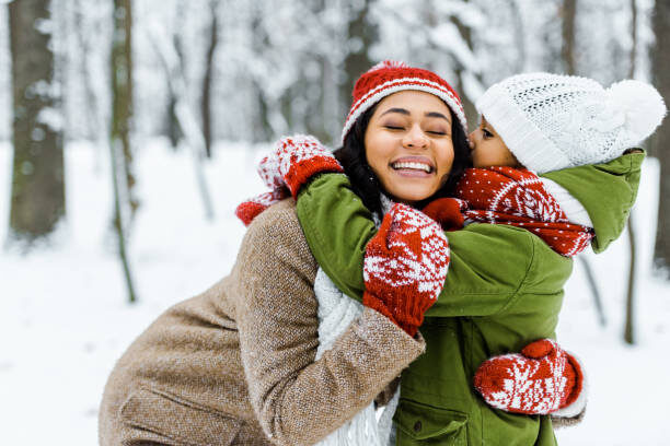 cute african american daughter hugging mother in winter forest